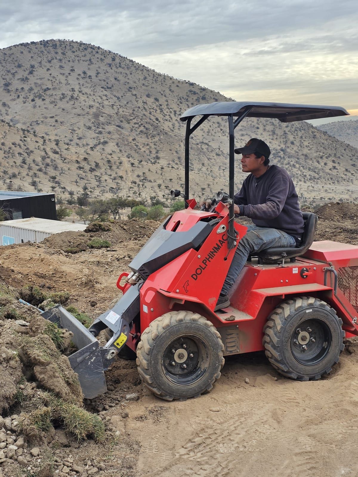 Minicargador S490 cargando material con balde, logo DolphinMac visible